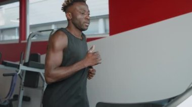 Modern spor salonunda koşu bandında koşan yakışıklı Afrikalı bir adam, orta boy portre, iyi sağlık ve his için yoğun kardiyo fitness çalışması, formda ve sportif bir vücut.