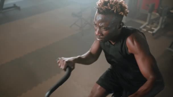 运动自行车在健身房里的积极锻炼 强壮的黑人男子是旋转踏板和移动式训练机的操纵杆 是锻炼身体 健康生活的健身中心 — 图库视频影像