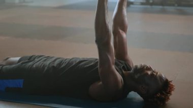 Spor salonunda güç çalışması, Afrikalı Amerikalı adam yerde yatıyor ve dambılları kaldırıyor, kol ve göğüs kaslarını geriyor, fitness merkezinde yoğun kardiyo eğitimi, sağlıklı yaşam tarzı ve spor hobileri.