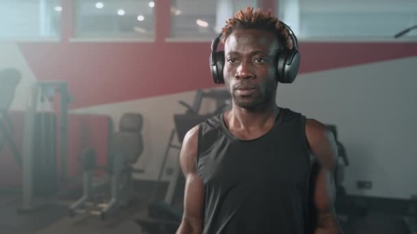 在健身房练习哑铃 描绘英俊的黑人男人举重 训练二头肌 锻炼胳膊和肩膀肌肉 在健身中心锻炼 用耳机听音乐 — 图库视频影像