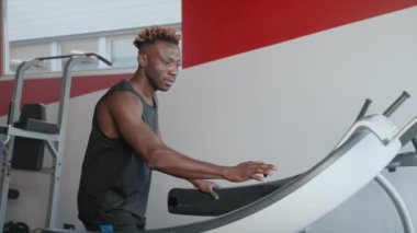 Kaslı siyah atlet spor salonunda koşu bandında koşuyor, modern fitness merkezinde kardiyo çalışması, dayanıklılık ve kardiyovasküler sistemi geliştiriyor, spor salonunda Afrikalı Amerikalı sporcu
