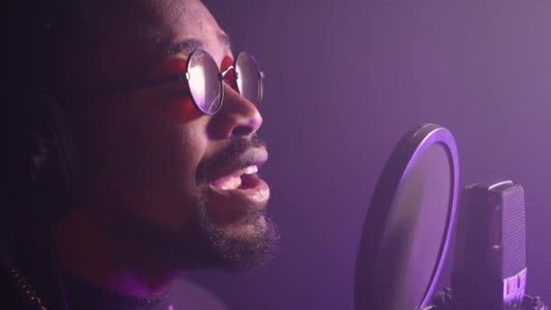 一个黑人闭着眼睛唱抒情歌曲的特写镜头 专业音乐家在录音室录制歌曲 在朦胧的紫光中拍摄 — 图库视频影像