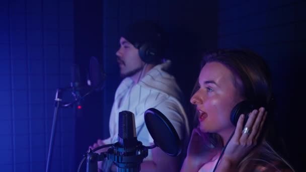 남녀가 마이크로 듀엣으로 노래를 부르면서 오디오 스튜디오에서 동작으로 새로운 노래를 — 비디오