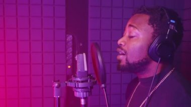 Profesyonel müzik üretimi. Yetenekli zenci şarkıcı yavaş bir aşk şarkısı söylüyor. Stüdyoda, renkli ışıkla.