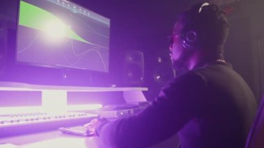 Bir müzik yapımcısının bilgisayar ve yazılım kullanarak yeni bir parça yaratırken yavaş çekim yapması, ekrandaki seçenekleri değiştirmesi ve kulaklıkla müzik dinlemesi. Karanlık uzayda mor ışık
