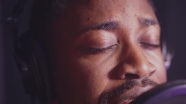 Profesyonel müzik stüdyosunda romantik bir aşk şarkısı söyleyen siyahi bir şarkıcının yavaş çekim çekimi. Gözlerini kapayan adam, heyecanla canlanıyor.