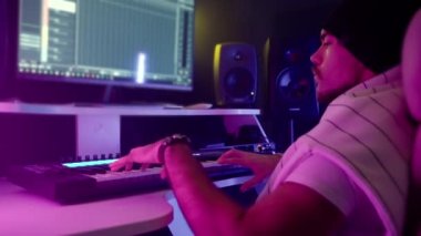 Müzisyen adam çağdaş kayıt stüdyosunda modern ekipmanlarla çalışıyor, dijital ses çalışma istasyonunda klavye çalıyor, çoklu monitör kurulumuna bakıyor, ses yönetmeni yeni hit şarkılar yaratıyor.