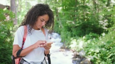 Yazın ormanda kaybolan genç bir kadın iletişim ve yön bulma için akıllı telefon kullanıyor. Yazın doğal parktaki kadın yürüyüşçünün portresi. Hafta sonu seyahat ediyor.