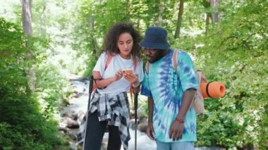 Yaz tatilinde ormanda yürüyüş yaparken elektronik rota haritasını gösteren iki yürüyüşçü, çok ırklı bir çiftin portresi, doğada seyahat eden iki arkadaş.