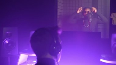 Profesyonel müzisyenler modern kayıt stüdyosunda albüm kaydediyorlar, yapımcı ve şarkıcı, havalı siyahi adam izolasyon kabininde şarkı söylüyor veya rap yapıyor, mikrofon ve kulaklık kullanıyor.