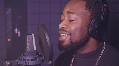 Profesyonel kulaklıklı Afro-Amerikan adam ses kayıt stüdyosunda yeni bir romantik pop şarkısı söylüyor. Yetenekli soul şarkıcısı yeni bir beste ve albüm yapıyor. Siyahi adamın portresi.