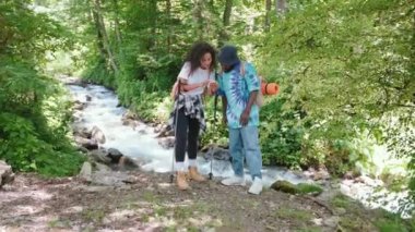 Akıllı telefondan arama yapan birkaç erkek ve kadın yürüyüşçü dağ nehri yakınlarındaki ormanda gezinti uygulamasında haritada rota buluyorlar. İskandinav usulü yaz yürüyüşü. Turizm, seyahat, yürüyüş konsepti.