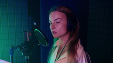 Slow motion shot of a woman speaking into a microphone in the audio studio to record the voiceover for movie, video or advertisement. Dubbing actor with script