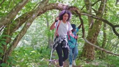 Explorers hikers couple diversity afroamerican man and woman hike in forest under tree branches practice nordic walk. Traveling trekking together. Tourism, travel, hiking, trekking, active recreation.