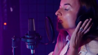 Slow motion close-up shot of a young sensual singer performing a song in recording studio with dim purple light. Professional music production