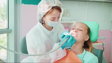 Diş hekimi dişçilikte dişçi kız için diş temizliği yapıyor. Stomatolog doktor stomatoloji kliniğinde dişlerini fırçalamak için profesyonel diş matkabı kullanıyor..
