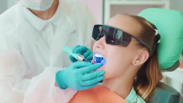 Tandläkare Installerar Ljushärdande Tätning Inom Tandvård Till Patient Tonåring Flicka — Stockvideo