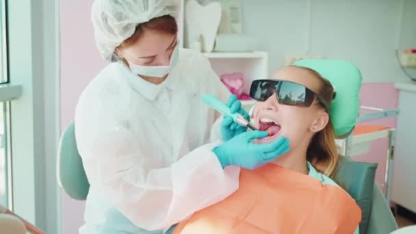 歯科医 十代の少女の歯に歯の充填をインストール ブルーライトを照らす キュレーションの近代的な技術とパルピス 子供のための歯科診療所での症候学者の任命 — ストック動画