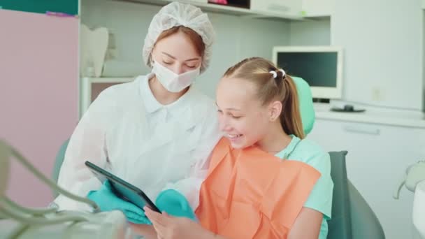 歯科医の女性と10代の少女患者 タブレットで子供の学習ビデオを示す医師 歯の衛生と健康についてのレッスン 中間の肖像画 — ストック動画