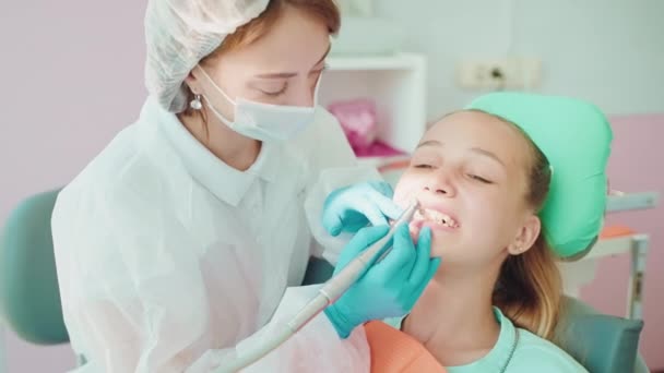 子供のための歯科診療所の専門の歯科クリーニング 女性歯科医が歯を磨くとき椅子に座っている10代の少女は 歯の病気と美しさを保存します — ストック動画