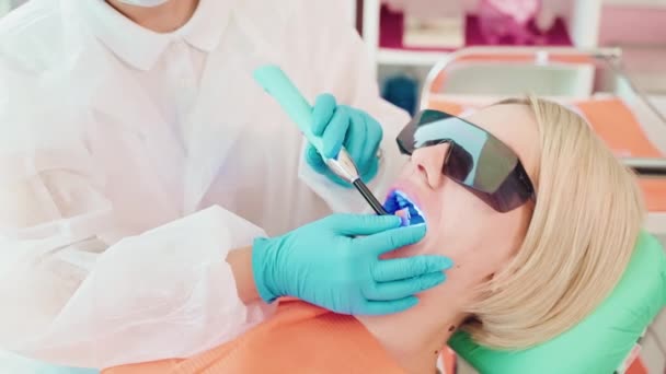 歯科医は 患者の女性に歯科にフォトポリマーシールを設置しています 気象学者は 紫外線を使用して 体外科クリニックで光硬化シールの重合を硬化させます キャビティ治療 — ストック動画