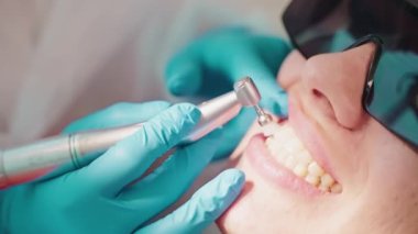 Stomatolog kadın dişçiliğinde hijyenik diş temizleme prosedürü uygular. Diş hekimi, stomatoloji kliniğinde dişlerini fırçalamak için profesyonel diş matkabı kullanıyor..