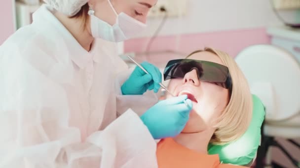 歯科医の診察 歯科診療所 椅子に座っているダークメガネの女性患者 医師は 彼女の歯を調べる 診断と治療のカレーと歯科インプラント — ストック動画