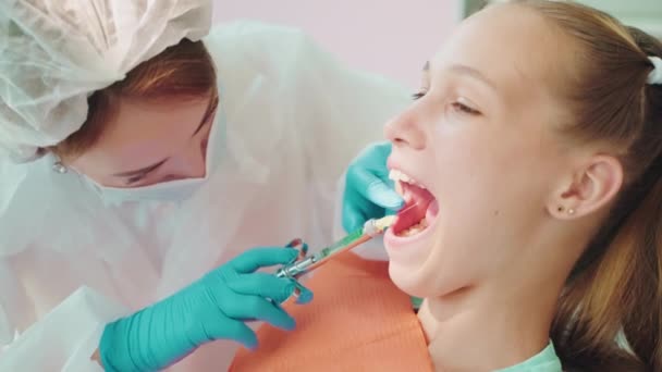 現代歯科の10代の少女に歯科麻酔を注入する麻酔薬を用いたシリンジを使用する歯科医 腸内科医の麻酔 歯科医院の口腔外科処置の前にガム — ストック動画