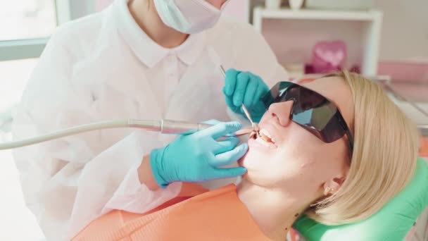歯科診療所の歯の専門的な衛生的なクリーニングの女性 歯を磨くために電気歯科ドリルマシンを使用する歯科医師 生理学者衛生士の医者はきれいな歯のプロシージャを作ります — ストック動画