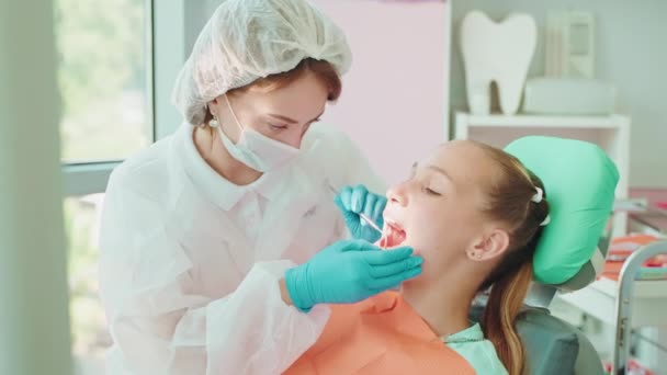 歯科の歯の診察を受けたティーンガール 歯科鏡を使って子供の歯を検査する歯科医の女性 ストーマトロジークリニックのティーンエイジャーのためのチェックアウトの実施 — ストック動画