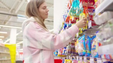 Marketten jöleli şeker alan kız vitrinin yanında duruyor. Abur cubur, lezzetli tatlılar hipermarkette paketlenmiş marmelat. Alış veriş, alışveriş, dükkan ve market konsepti..