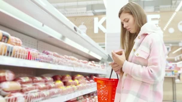 Młoda Zainteresowana Kobieta Wybiera Kiełbasę Supermarkecie Dziale Mięsnym Supermarkecie Dziewczyna — Wideo stockowe