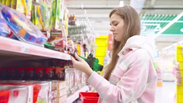 年轻的金发母亲选择在超级市场为儿子购买塑料玩具枪 女人看着超市里手牵手的塑料玩具 妈妈准备礼物 给孩子的惊喜 购物概念 — 图库视频影像