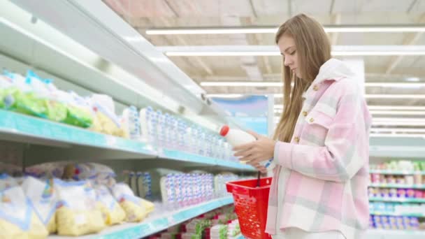 女买方在商场的乳制品食品部选择购买奶瓶 超市里的购物杂货从橱窗里放进篮子里 超级市场概念下的食品店 — 图库视频影像