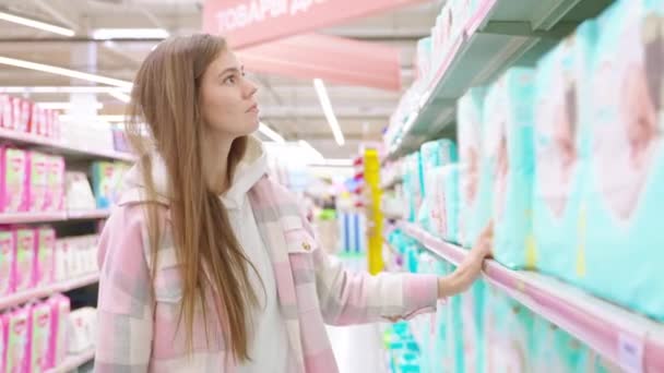 困惑的金发年轻妈妈选择在超级市场为新生婴儿买尿布 妇女妈妈在超级市场为孩子做皮箱 幼儿保育 母婴保健用品概念 — 图库视频影像