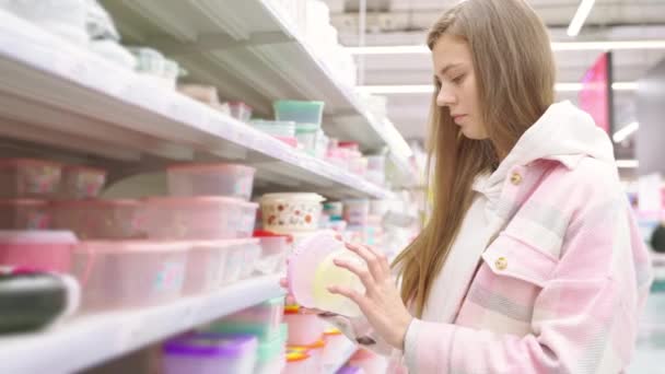 超级市场的年轻女购物者 走道上拿着餐具的妇女画像 女士看塑料食品容器以节省和带走 检查使用的质量和舒适性 — 图库视频影像