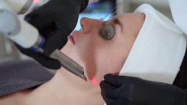 Kadın kozmetoloji kliniğinde lazer gençleştirme tedavisi sırasında dinleniyor, estetikçi kılcal damarların pıhtılaşması ve modern güzellik teknolojisi için lazerle çalışıyor.