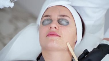 Kozmetoloji ve cilt bakımı kliniğinde yüz derisini tedavi eden güzellik uzmanı, kadın yüzüne jel sürüyor, cilt bakımı ve yaşlanma karşıtı, akne önleyici prosedürler uyguluyor