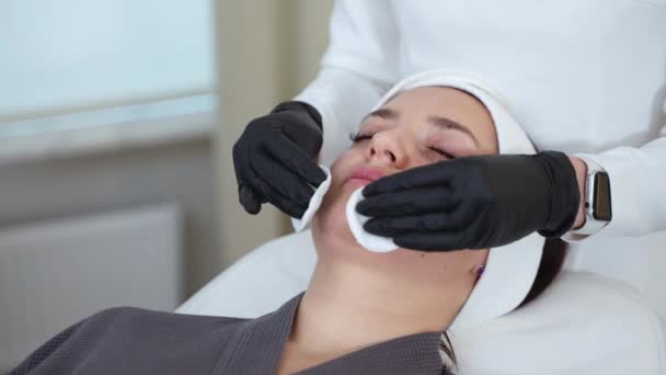 美容师在美容院用棉垫清洁一位女顾客的脸 面部处理与护肤产品 — 图库视频影像
