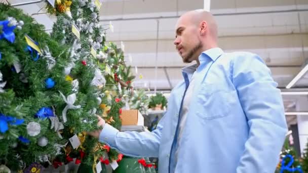 クリスマスの休日に店で買うハンサムな男 Xmasおよび新年のための家の装飾を選ぶ大人の男性の店 スーパーマーケットでクリスマス リースを買う顧客 — ストック動画