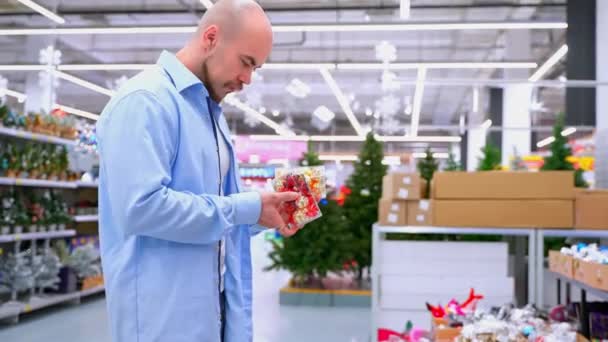 Mann Kauft Vor Weihnachten Geschäft Ein Männlicher Käufer Wählt Weihnachtsbaumschmuck Stock-Filmmaterial