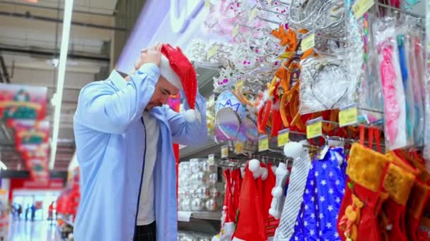 Mann Probiert Nikolausmütze Geschäft Einkauf Supermarkt Vor Weihnachten Und Neujahr Stock-Filmmaterial
