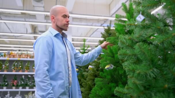 男人在商店里挑人造圣诞树 男人在圣诞节和新年前挑装饰品 准备过冬 — 图库视频影像