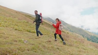 Aktif giyimli ve spor ayakkabılı iki kişi dağlarda birlikte yürüyorlar, erkek ve kadın dağ yamaçlarında İskandinav yürüyüşü yapıyorlar, hafta sonları aktif ve sportif eğlence, sırt çantaları ve yürüyüş