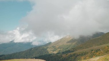 Yeşil dağları ve güneşli bir günde tepeleri kaplayan bulutları olan inanılmaz manzaralı bir doğa. Turistler için seyahat güzergahları. Turistik bir yer. Ormana, çayıra, tarlaya sinematik bakış.