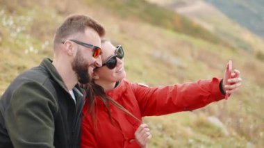 Doğada akıllı telefonla selfie çeken genç gezginler, dağ zirvesine çıktıktan sonra dinlenen erkek ve kadın, turizm ve tatilde ve hafta sonunda doğal güzellikte seyahat eden güzel gezginler.