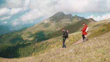 Turizm ve dağ gezisi, yüksek dağların yamacında birlikte yürüyen iki turist, arka planda inanılmaz doğal manzara, ekolojik alanlarda seyahat, doğa yürüyüşleri ve sırt çantaları