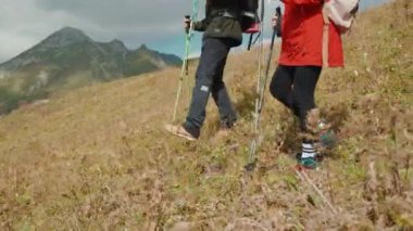 Bir çift yürüyüşçü erkek ve kadın dağdan aşağı iniyor ellerinde İskandinav çubukları, bacaklarında yakın plan. Gezginler birlikte dağlarda yürüyüş yapan turistler. Vahşi doğada gezintiye çıktım..