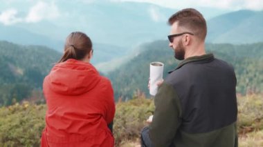 Termostan çay içen turist erkek, dağ vadisine hayran olarak oturuyor. Gezginler tatilde ailelerini dağlarda gezdirirler. İnsanlar vahşi doğa hakkında konuşuyor..