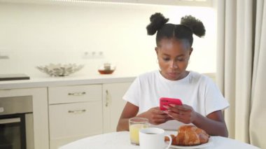 Siyah kadın kahvaltıda akıllı telefonla sohbet ediyor, internet bağımlısı kadın portresi, sosyal medyayı izleyen Afrikalı Amerikalı kadın ve mobil uygulama kullanıyor.